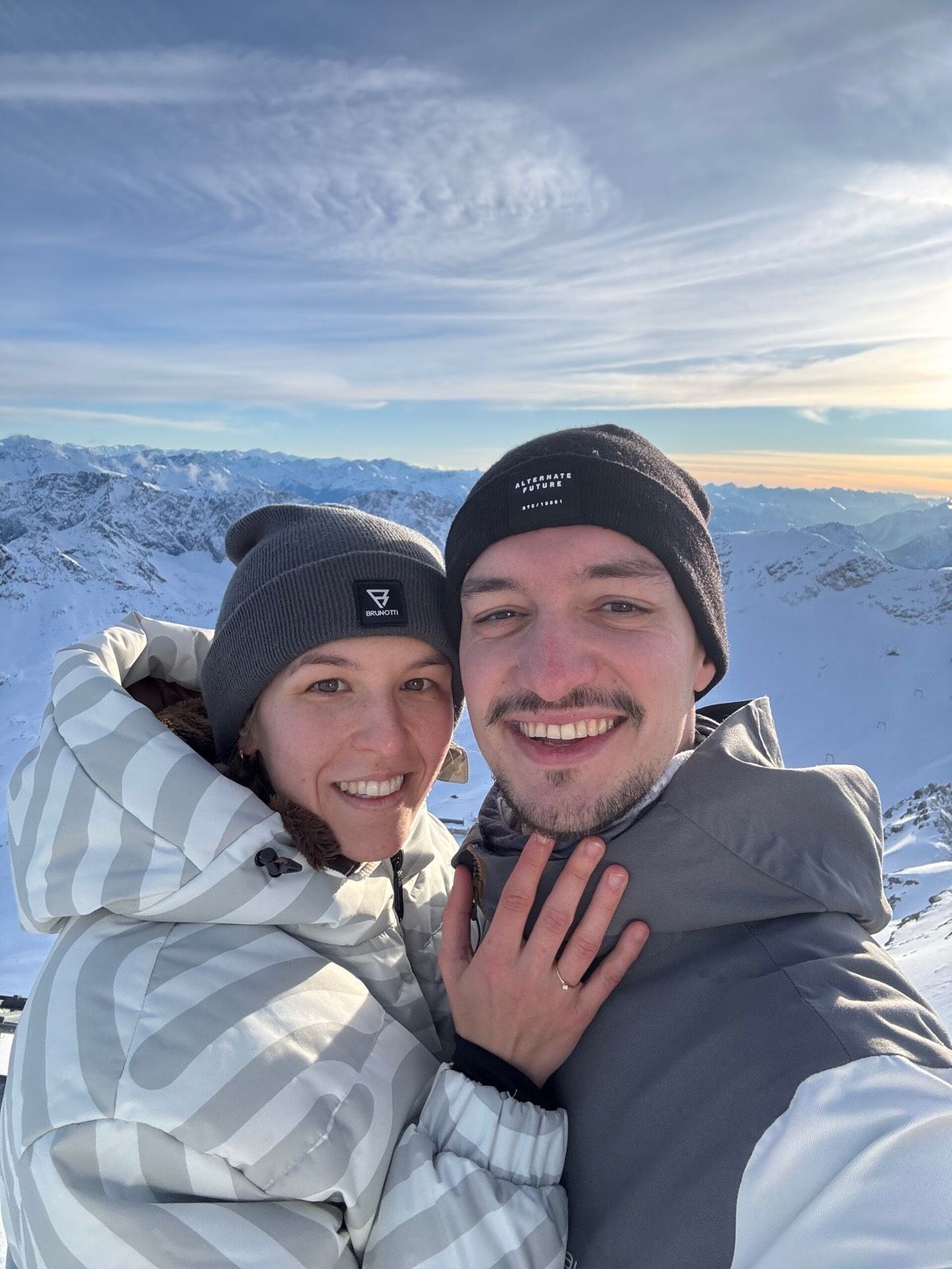 Selfie von Vicky und Alex im Schnee auf einem Berggipfel, Vicky zeigt ihren Verlobungsring